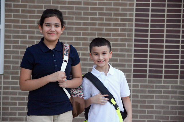 a girl and a boy student standing in front of las colinas elementary with their backpacks on