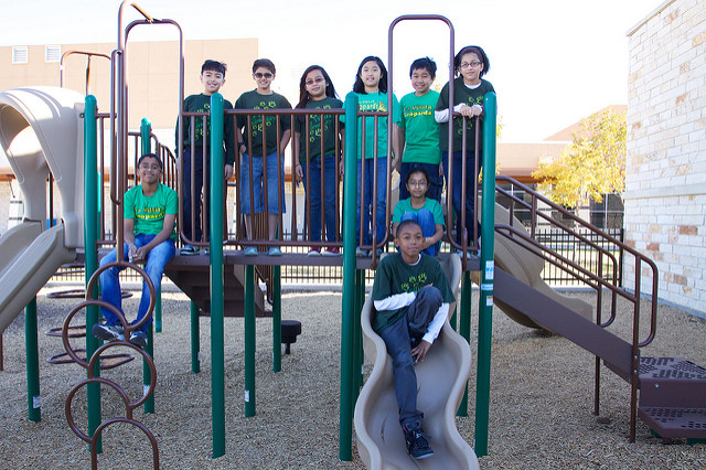 9 students posing for a picture on a playground with green shirts. 