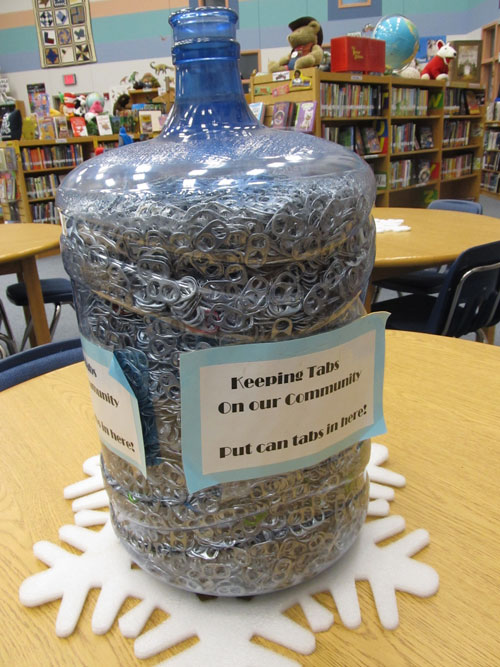 a liter water jug full of can tabs with a sign on it that says Keeping tabs on our community, put can tabs in here!