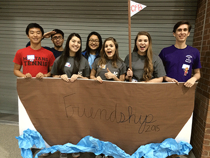 7 students holding a hand made paper ship that says "friendship 2015"