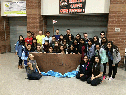 7 students holding a hand made paper ship that says "friendship 2015"