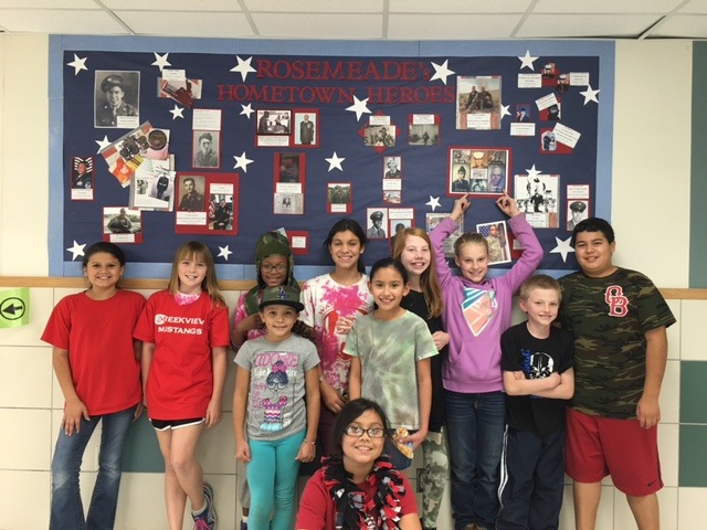 A group of students in front of a banner with pictures that says Rosemeade's Hometown Heroes