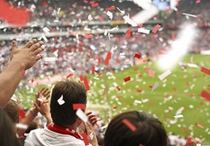 fans at a soccer game cheer on the crowd. They are clapping and throwing red and white confetti